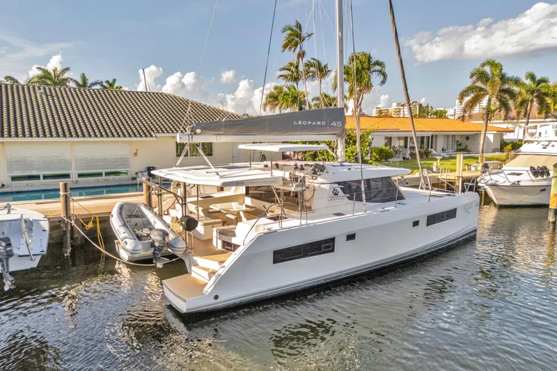  Yacht Photos Pics 2020 Leopard 45 catamaran docked by waterfront homes, surrounded by palm trees.