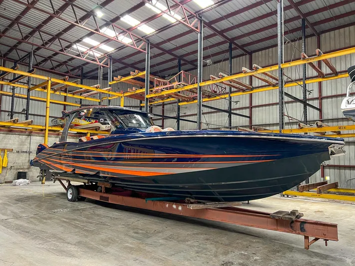 Thunder Struck Yacht Photos Pics 2024 MTI V42 boat in warehouse, sleek design with orange and blue accents.