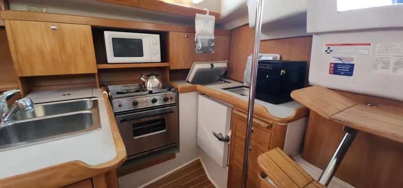 Janice Marie Yacht Photos Pics 2004 Catalina 350 Sloop kitchen with stove, microwave, sink, and wooden cabinetry.
