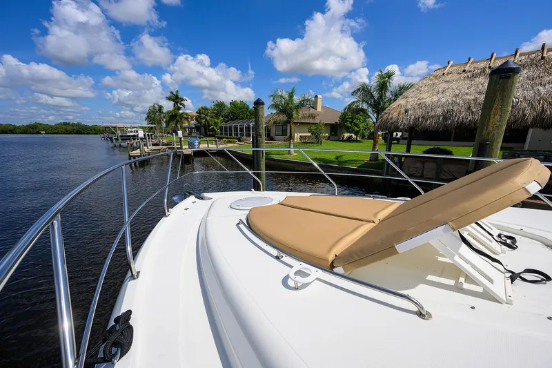 Ajac Cruiser Yacht Photos Pics 2015 Cruisers Cantius yacht with sunbed, docked by a scenic waterfront with palm trees and blue sky.