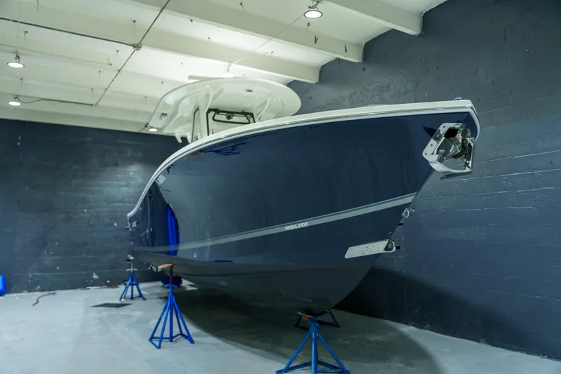  Yacht Photos Pics 2023 Regulator 28 boat in a showroom, elevated on stands, with a sleek blue hull.