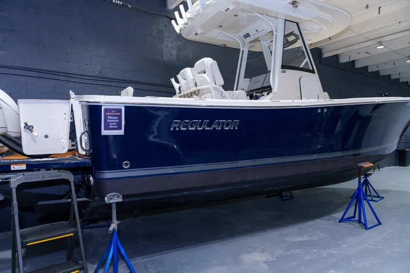  Yacht Photos Pics 2023 Regulator 28 boat in showroom, blue hull, elevated on stands.