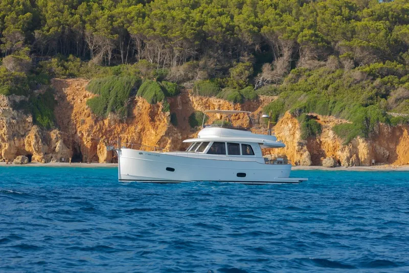 Yacht Photos Pics 2026 Sasga Yachts 55 cruising near rocky coastline with lush greenery.