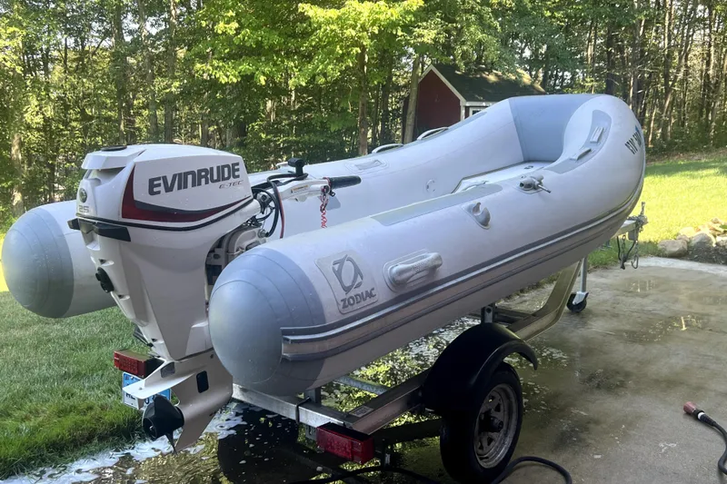  Yacht Photos Pics Inflatable Zodiac boat with Evinrude motor on trailer, outdoors in a wooded area.