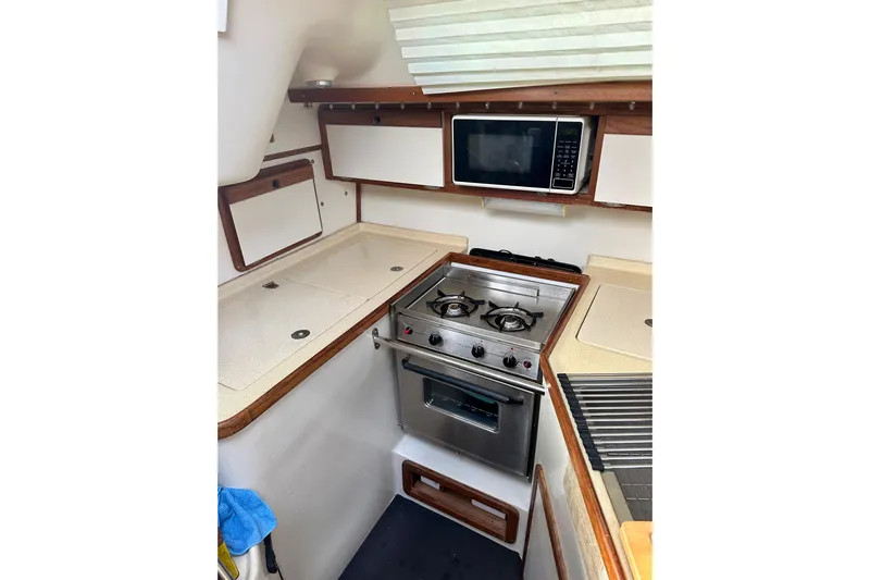Makai Yacht Photos Pics Compact kitchen in 1999 Catalina 320 sailboat with stove, microwave, and storage cabinets.