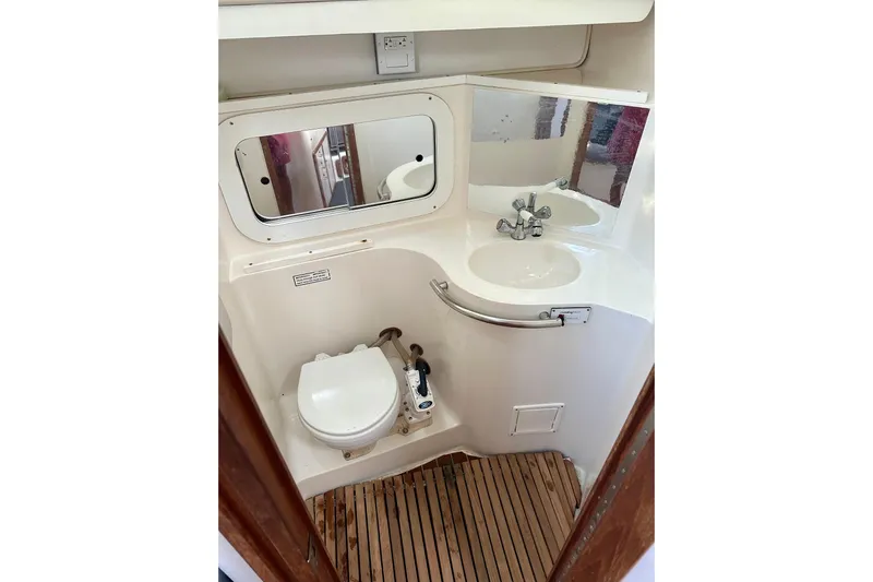 Makai Yacht Photos Pics 1999 Catalina 320 yacht bathroom with toilet, sink, mirror, and wooden floor.