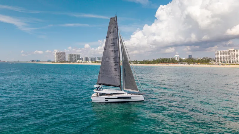 Noble House Yacht Photos Pics 2019 McConaghy MC60 sailing near a coastal city under a partly cloudy sky.