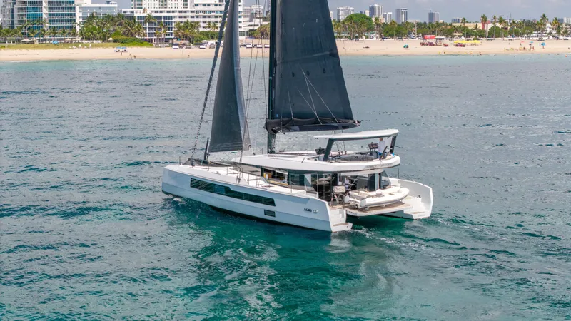 Noble House Yacht Photos Pics 2019 McConaghy MC60 catamaran sailing near a beach with city skyline backdrop.