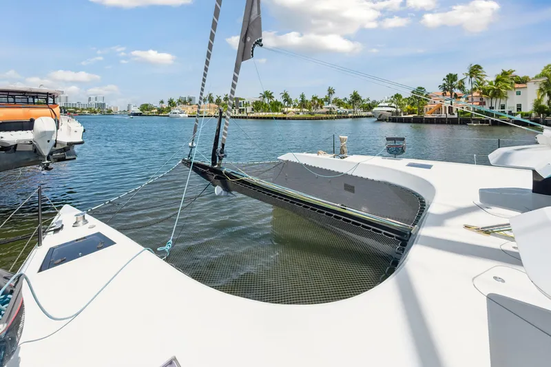 Noble House Yacht Photos Pics 2019 McConaghy MC60 catamaran on a sunny waterfront with palm trees and boats.