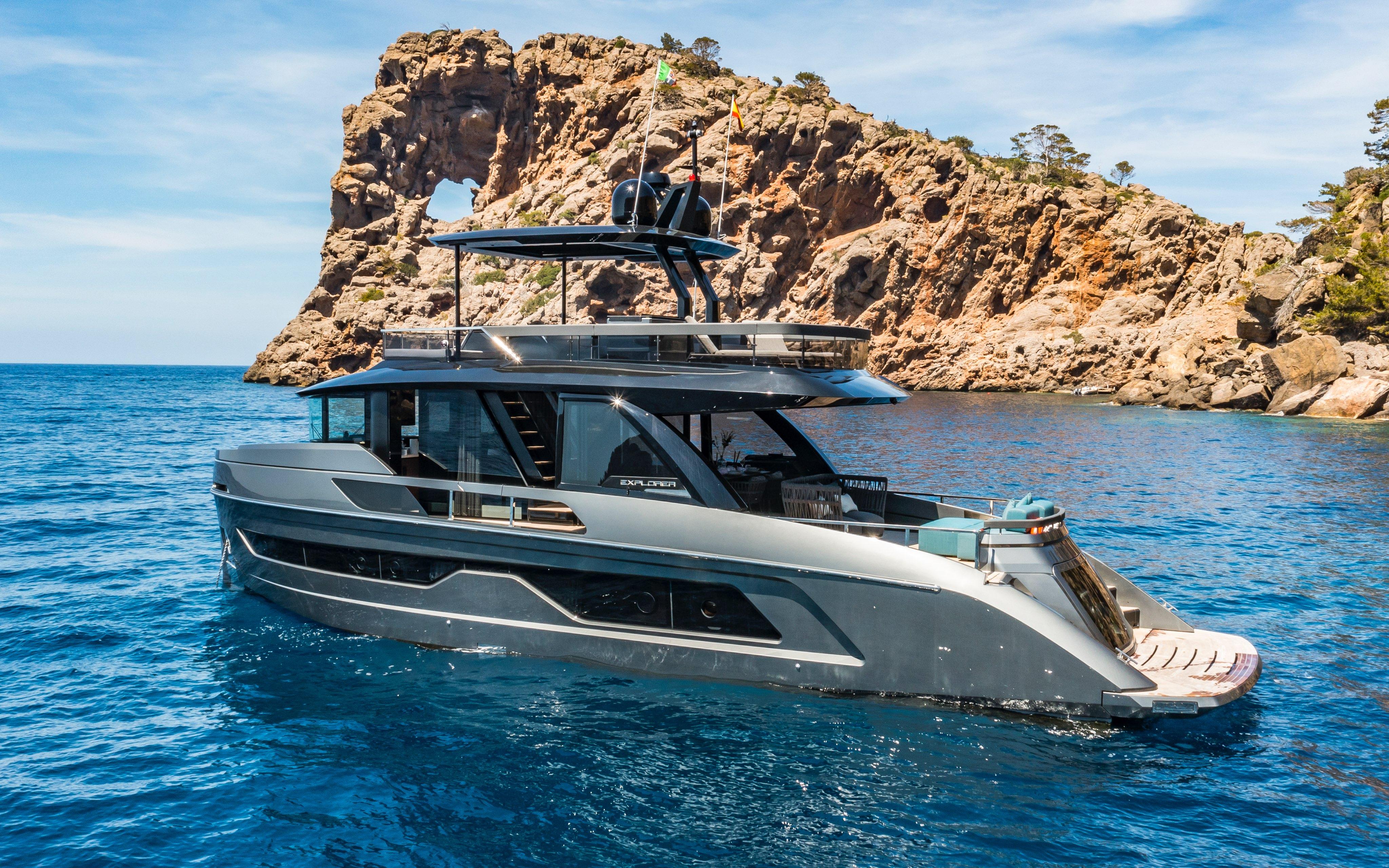 Luxurious 2025 Explorer 62 yacht cruising near rocky coastline under clear blue skies.