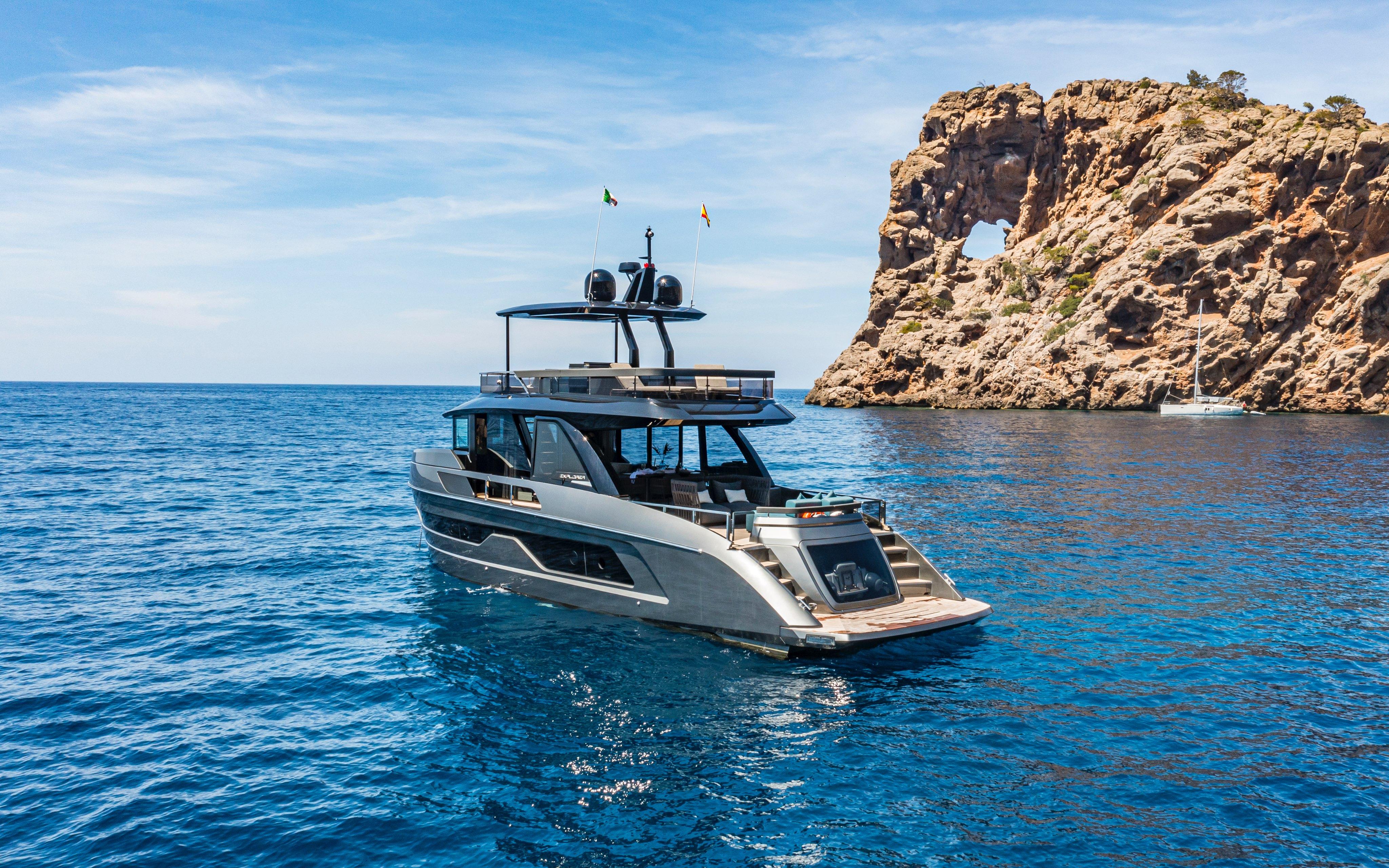 2025 Explorer 62 yacht cruising near a rocky coastal formation under a clear blue sky.