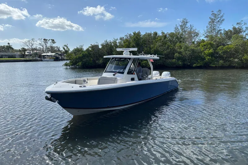  Yacht Photos Pics 2023 Pursuit S 328 Sport boat on calm water, surrounded by lush greenery.