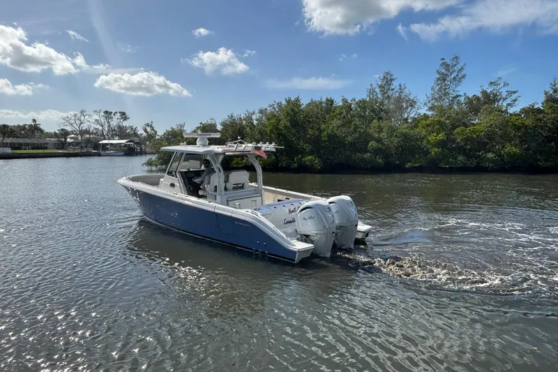  Yacht Photos Pics 2023 Pursuit S 328 Sport boat cruising on a calm river under a clear blue sky.