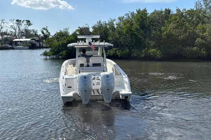  Yacht Photos Pics 2023 Pursuit S 328 Sport boat navigating a calm river, surrounded by lush greenery.