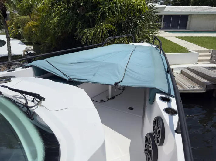  Yacht Photos Pics 2023 Axopar 28 T-Top boat with blue cover, docked near lush greenery.