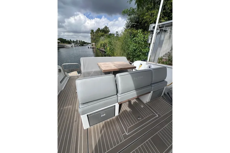 No Name Yacht Photos Pics 2024 Pardo Yachts P38 deck with seating and table, docked by lush greenery.