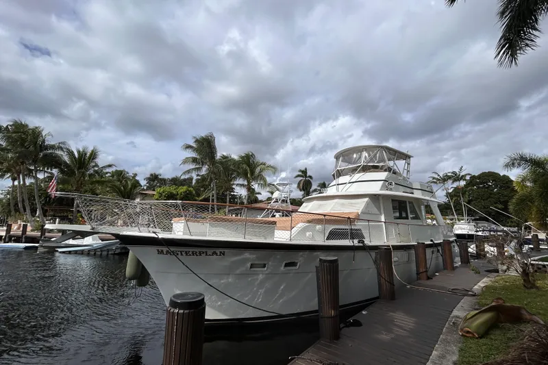 Masterplan Yacht Photos Pics 1975 Hatteras 58 YF yacht docked, surrounded by palm trees and cloudy sky.