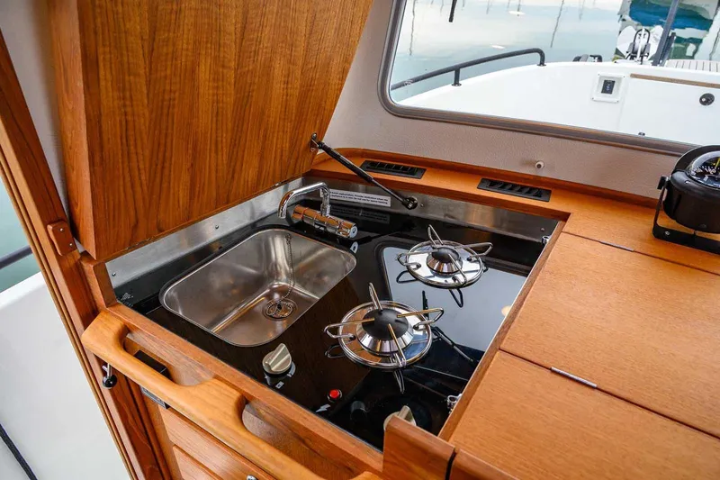  Yacht Photos Pics 2024 Targa 27.2 boat kitchen with stove and sink, featuring wooden cabinetry.