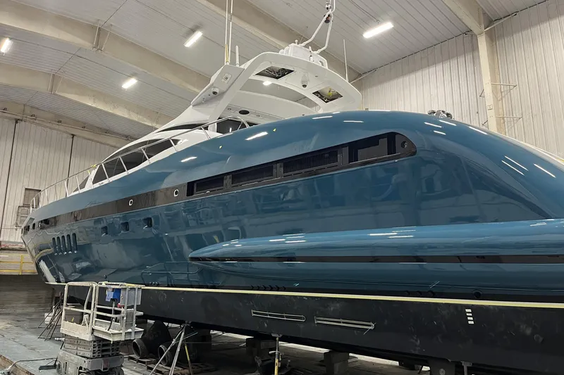 Olivia K Yacht Photos Pics Mangusta 92 yacht from 2005 in a shipyard, showcasing sleek design and blue hull.