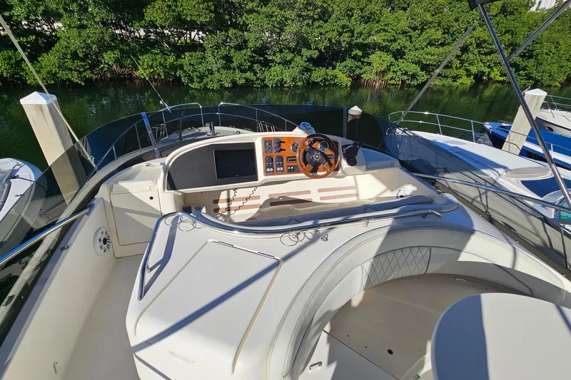 Kopara Yacht Photos Pics Cockpit of 2005 Prestige 46 yacht with steering wheel and control panel, docked by lush greenery.