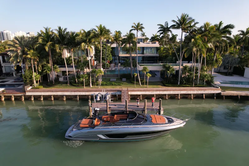 Grey Yacht Photos Pics 2021 Riva 56 Rivale yacht docked by a luxurious waterfront villa with palm trees.