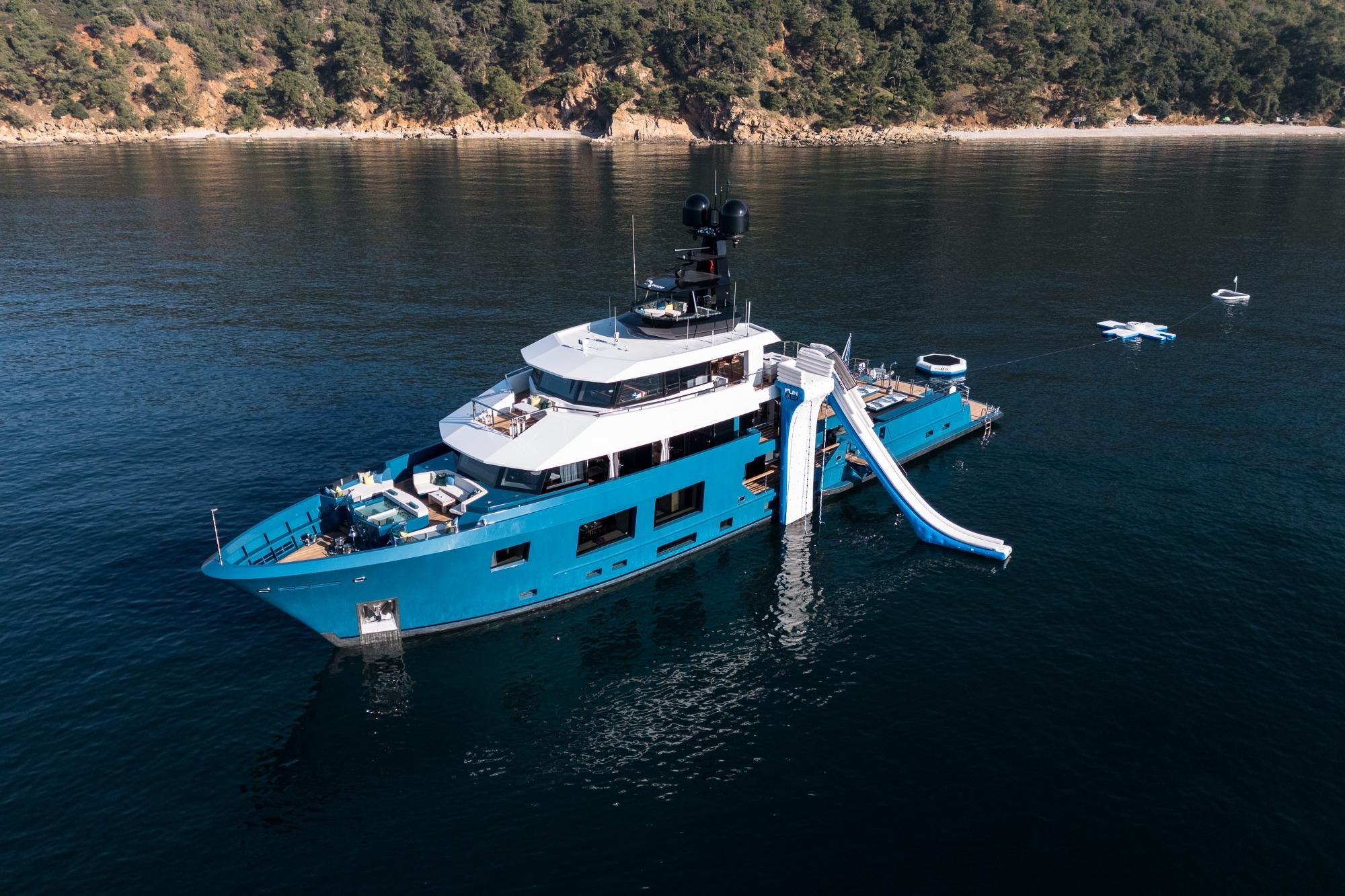 2024 Dunya Yachts Explorer with slide, anchored in serene waters near a forested coastline.