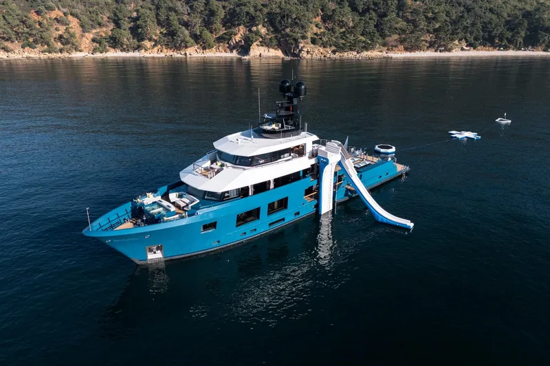 King Benji Yacht Photos Pics 2024 Dunya Yachts Explorer with slide, anchored in serene waters near a forested coastline.