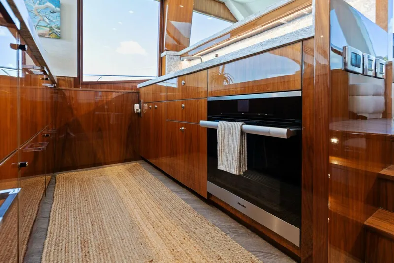 Mana Yacht Photos Pics Luxurious kitchen interior of 2021 Viking 82 Cockpit Motor Yacht with wood cabinetry and modern appliances.