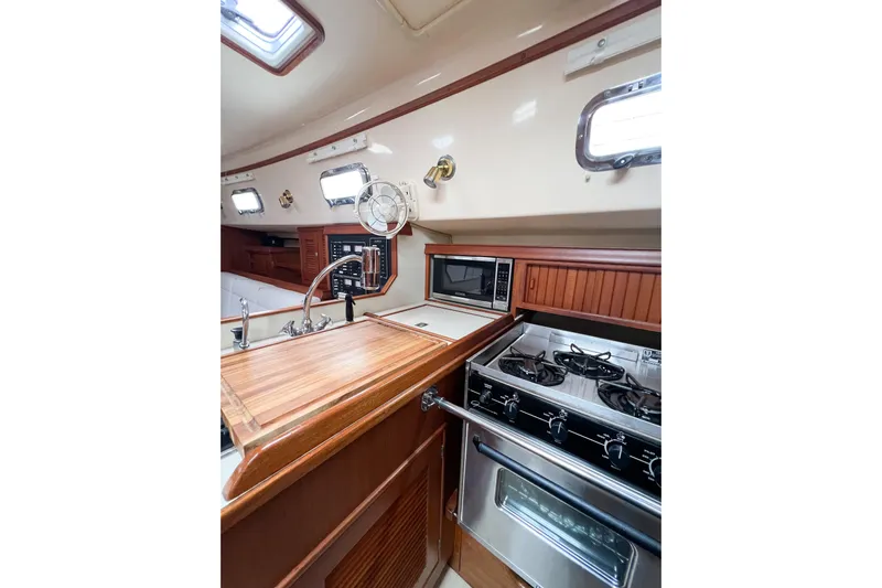 Delicia Yacht Photos Pics 1995 Island Packet 40 yacht interior kitchen with stove, microwave, and wooden cabinetry.
