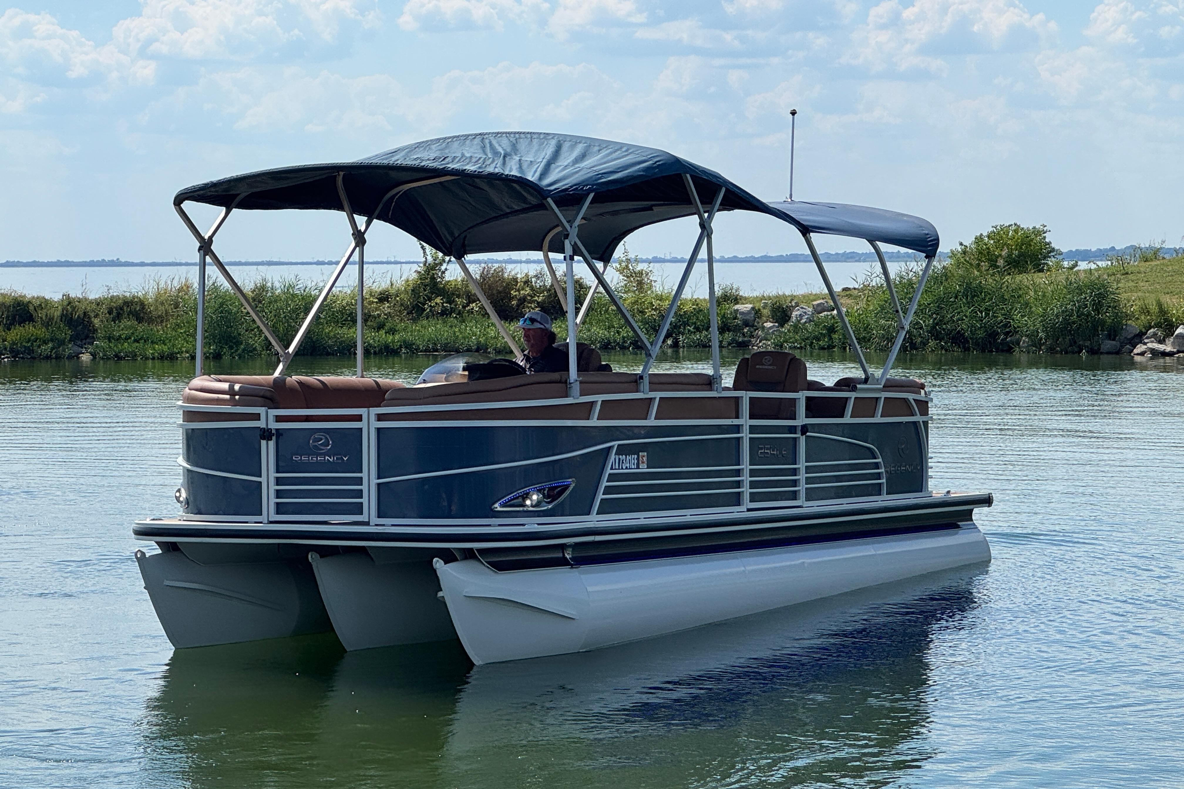 2017 Regency 254 LE3 pontoon boat on a calm lake with canopy.