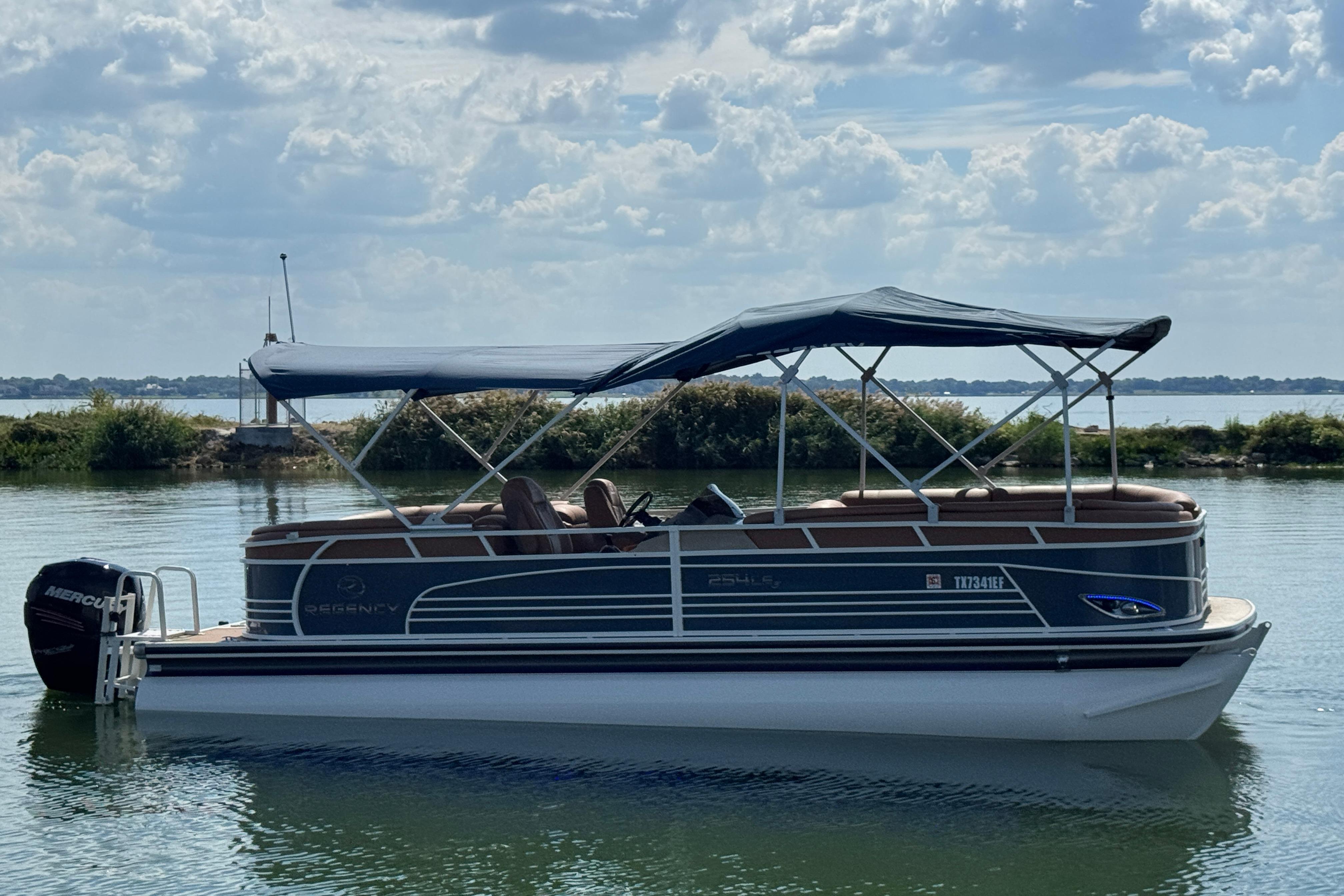 2017 Regency 254 LE3 pontoon boat on calm water with canopy and Mercury outboard motor.