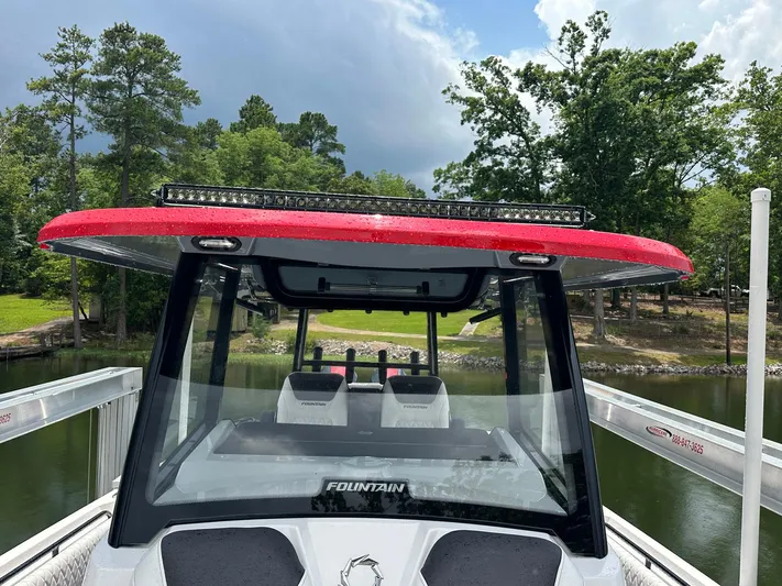  Yacht Photos Pics 2024 Fountain 32 NX boat with red roof, docked by a scenic lake.