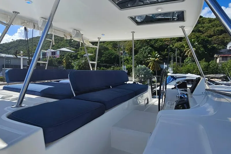 Artemis Yacht Photos Pics 2023 Lagoon 46 yacht with blue seating, docked near lush greenery and buildings.