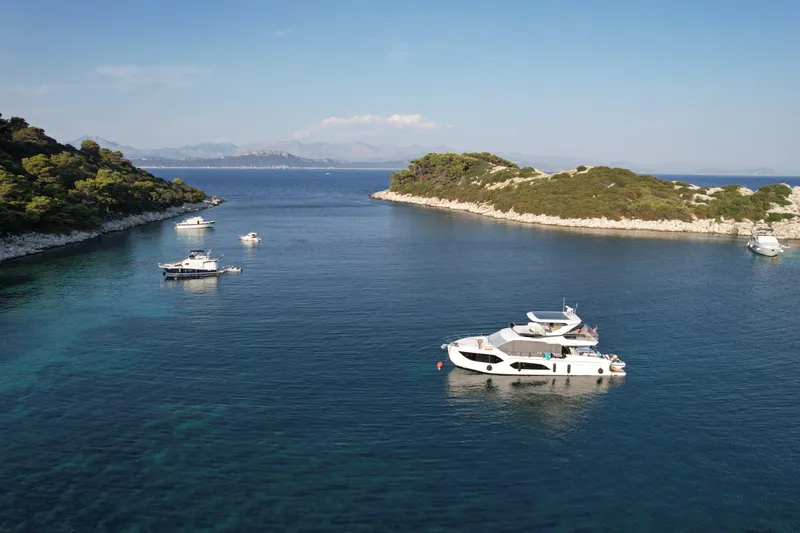  Yacht Photos Pics 2024 Absolute 60 Fly yacht anchored in a serene coastal bay with other boats.