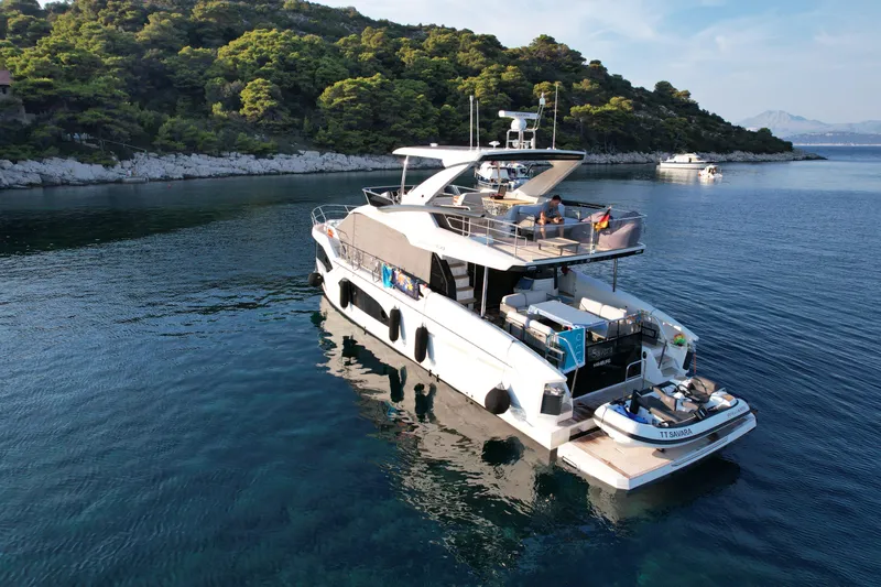  Yacht Photos Pics 2024 Absolute 60 Fly yacht anchored in serene, clear waters near a lush, green island.