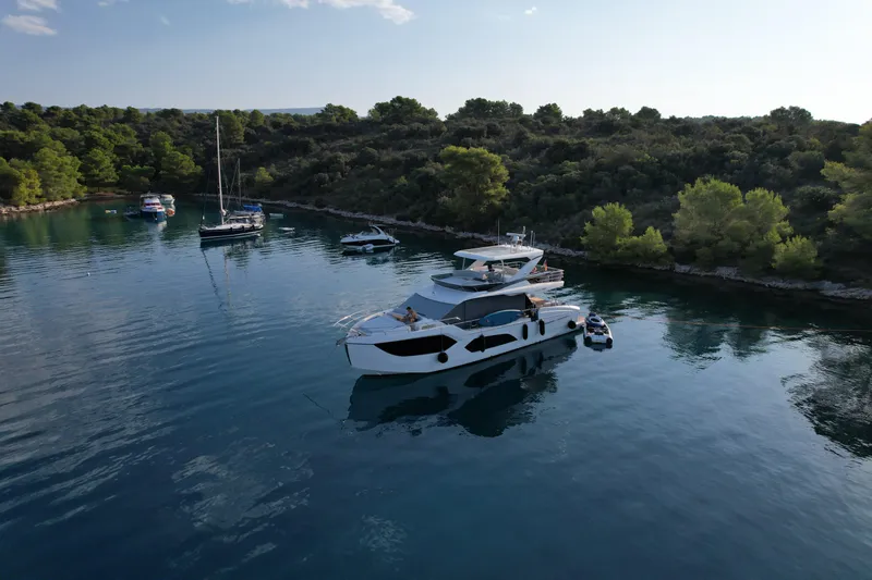  Yacht Photos Pics 2024 Absolute 60 Fly yacht anchored in serene, tree-lined bay with other boats.