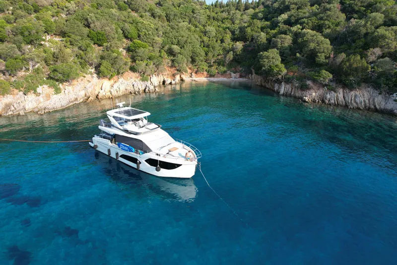  Yacht Photos Pics Luxurious 2024 Absolute 60 Fly yacht anchored in a serene, turquoise bay.