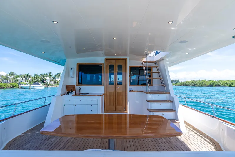 Tonic Yacht Photos Pics Luxurious 2018 Grand Banks GB60 yacht deck with wooden table and stairs, overlooking serene waters.