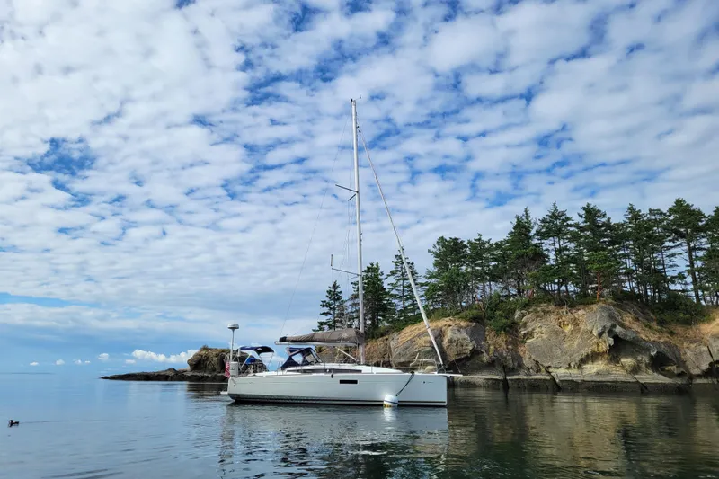 Imagine Yacht Photos Pics 2017 Jeanneau Sun Odyssey 349 sailboat anchored near rocky shoreline under cloudy sky.