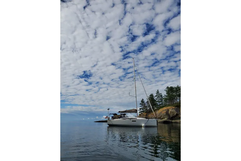 Imagine Yacht Photos Pics 2017 Jeanneau Sun Odyssey 349 sailboat anchored near rocky shoreline under cloudy sky.