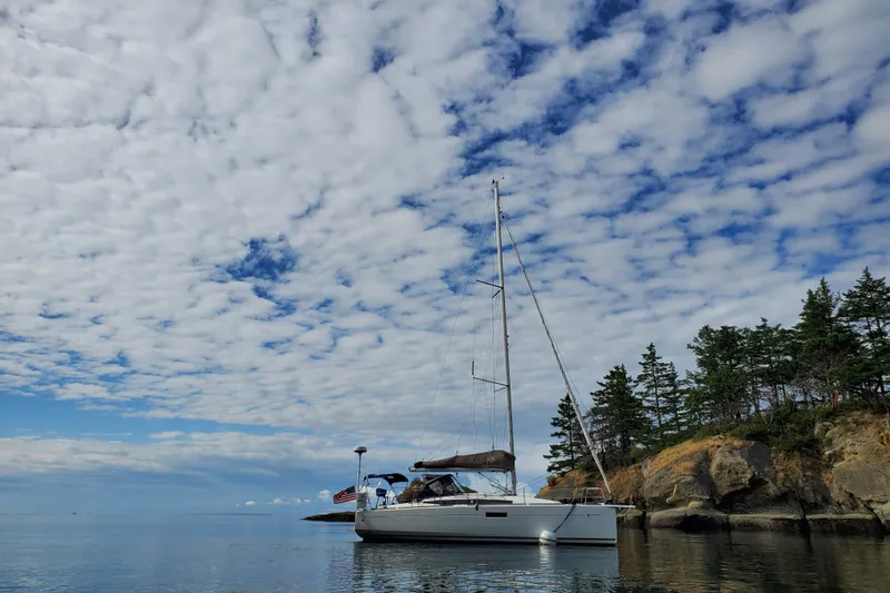 Imagine Yacht Photos Pics 2017 Jeanneau Sun Odyssey 349 sailboat anchored near rocky shoreline under cloudy sky.