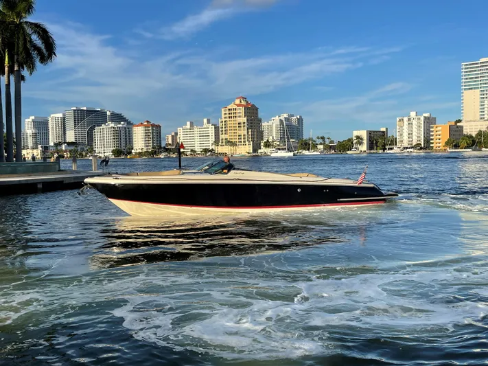 Grato Yacht Photos Pics 2015 Chris-Craft 32 Launch boat cruising near city skyline on a sunny day.