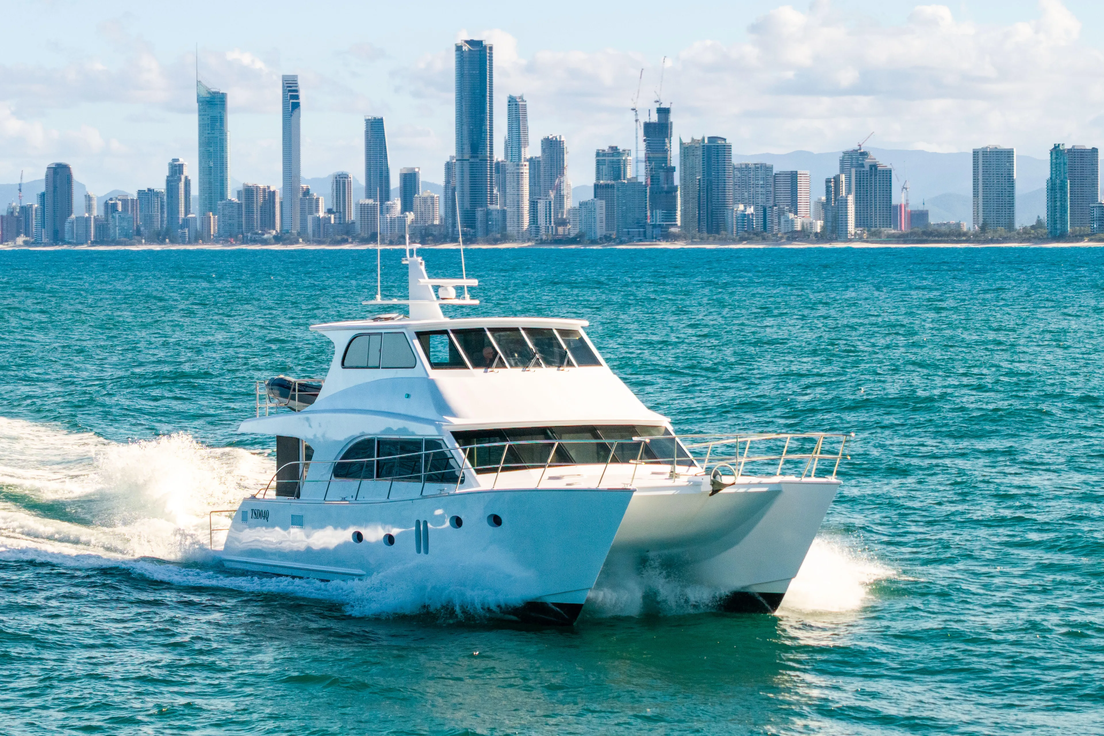 One Off Yacht Photos Pics 2019 Coral Coast 62 Power Catamaran cruising near city skyline on blue ocean waters.