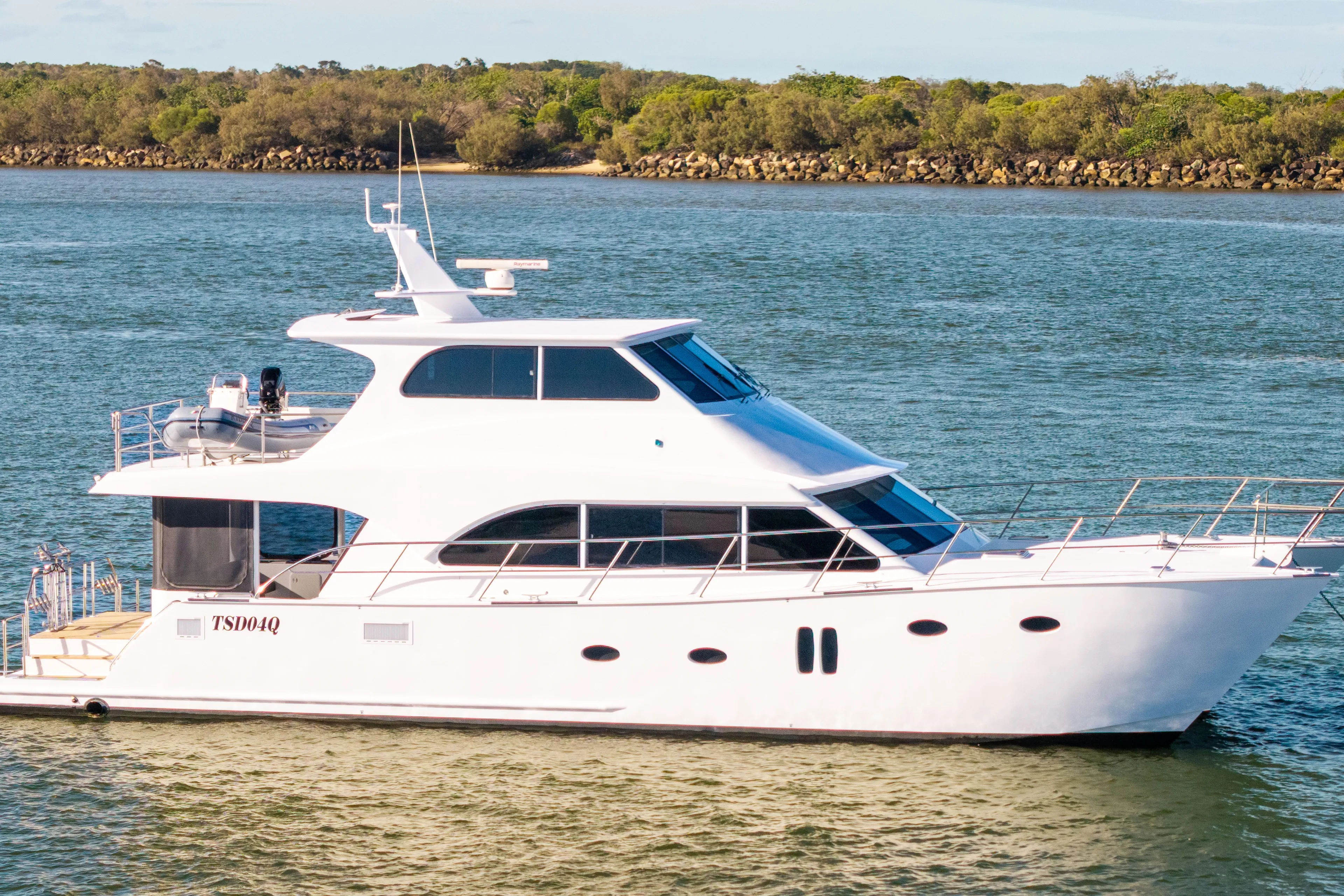 One Off Yacht Photos Pics 2019 Coral Coast 62 Power Catamaran cruising on calm waters near a lush shoreline.