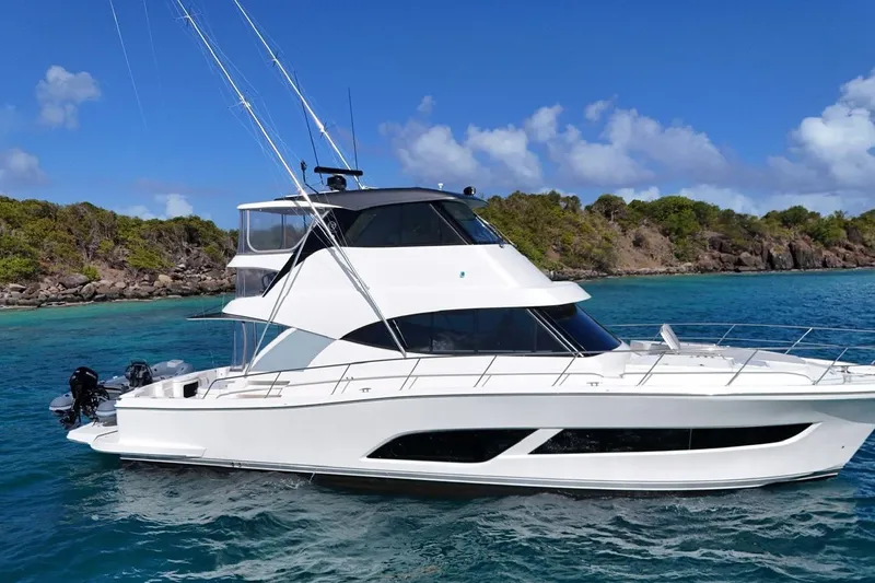  Yacht Photos Pics 2021 Riviera 50 Sports Motor Yacht cruising in clear blue waters near a rocky shoreline.