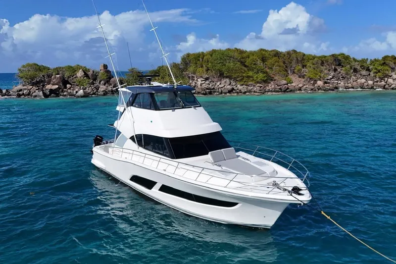  Yacht Photos Pics 2021 Riviera 50 Sports Motor Yacht anchored in clear blue waters near a rocky island.