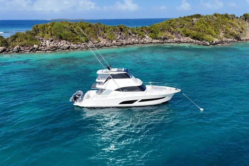  Yacht Photos Pics 2021 Riviera 50 Sports Motor Yacht anchored in clear turquoise waters near a lush island.