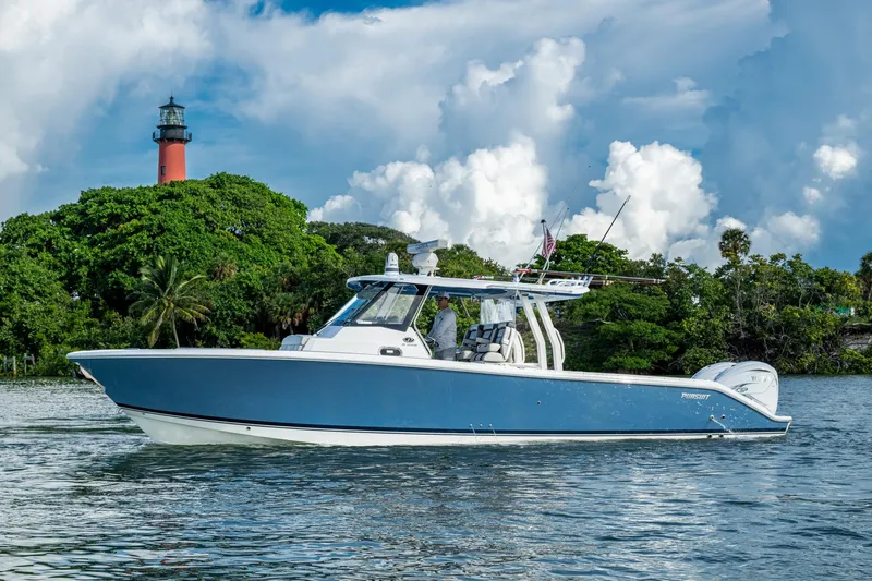 Island Girl II Yacht Photos Pics 2023 Pursuit S 358 Sport boat on water near lush greenery and lighthouse.