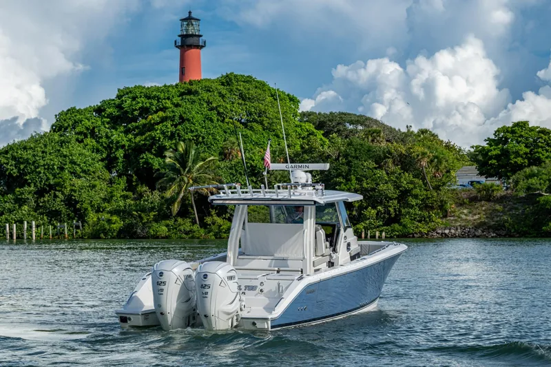 Island Girl II Yacht Photos Pics 2023 Pursuit S 358 Sport boat cruising near a lush island with a lighthouse.