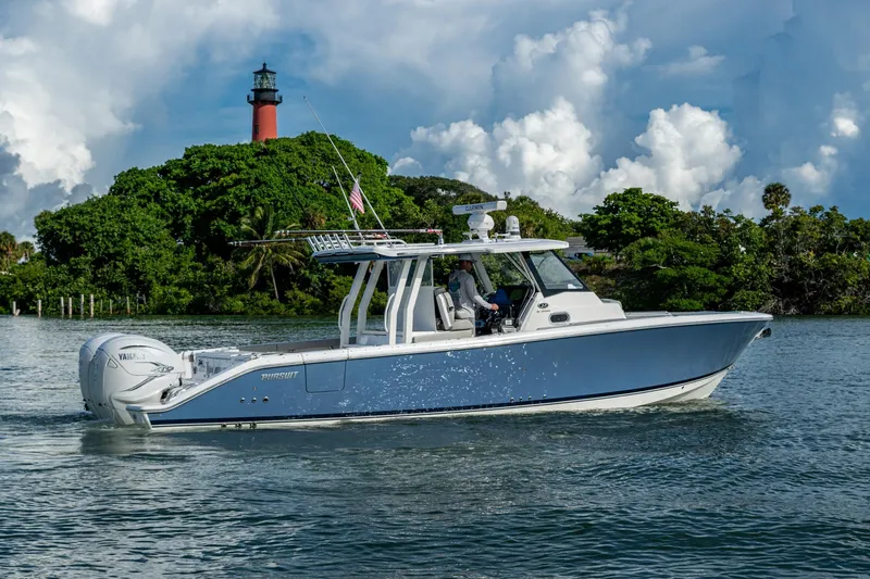 Island Girl II Yacht Photos Pics 2023 Pursuit S 358 Sport boat cruising near a lush island with a lighthouse.